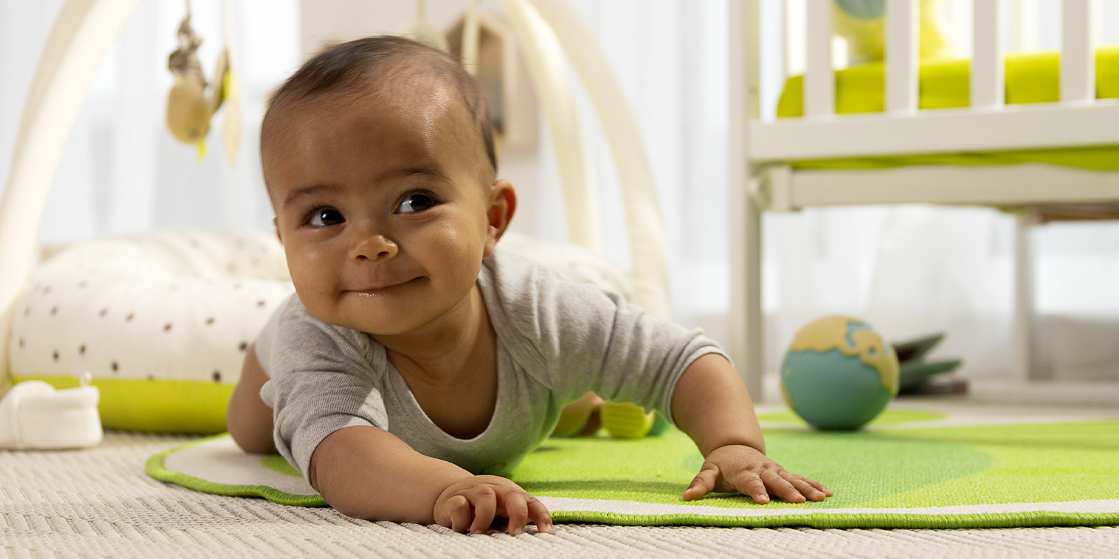 Un bébé en situation sur son lieu de mode de garde. Le Bébé allongé sur le ventre sur un tapis d'éveil Wesco et qui sourit - le blog wesco