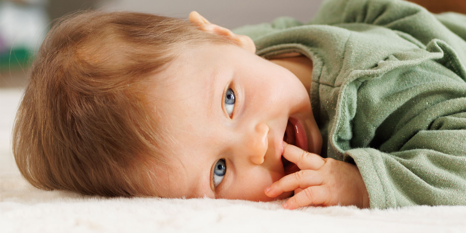 bebe 12 mois allongé sur un tapis au sol avec un regard espiègle blog wesco